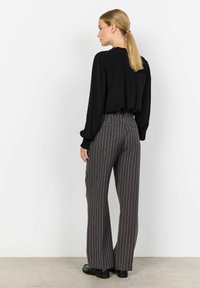 Blusa negra de manga larga con cuello acampanado combinada con pantalones grises de rayas, de cintura alta. Textura suave, corte relajado. Calzado negro.