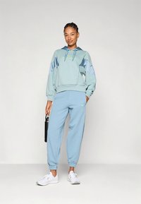 Γαλάζιο φούτερ με κουκούλα και αντίθετες επιφάνειες, συνδυασμένο με τζόγκερς στο ίδιο χρώμα. Λευκά αθλητικά παπούτσια και μια μαύρη παγούρι νερού ολοκληρώνουν την εμφάνιση.