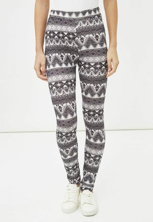 Leggings de estampado en blanco y negro con diseños geométricos, cintura elástica y corte ajustado, combinados con zapatillas deportivas blancas.