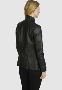 Black leather jacket with a fitted design, high collar, and smooth texture. Features seam detailing and a sleek, contemporary silhouette.