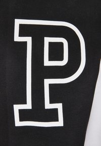 Schwarzer Stoff mit einem großen weißen, umrandeten Buchstaben "P", der darauf gedruckt ist, wahrscheinlich Teil eines Kleidungsstücks oder Textils.