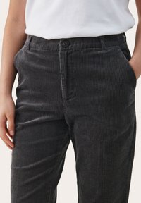 Pantalon en velours côtelé gris avec une texture à côtes verticales, une taille avec un bouton de fermeture et des poches latérales. Associé à une chemise blanche.