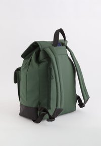 Mochila de tela verde con una forma estructurada, correas acolchadas y una base negra. Cuenta con cremalleras y un asa superior para mayor comodidad.
