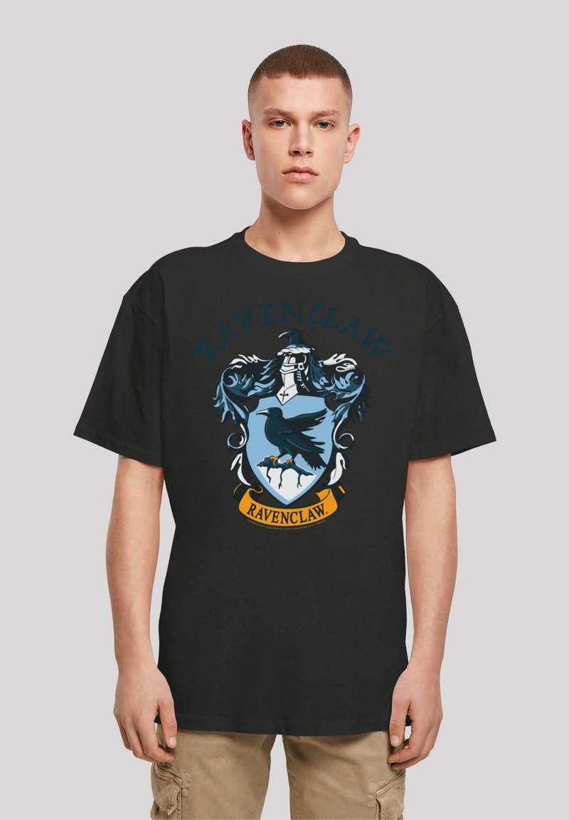 Camiseta de algodón negra con un diseño del escudo de Ravenclaw en azul y blanco que lleva el texto "RAVENCLAW" en la parte superior y una banda en la parte inferior. Manga corta.