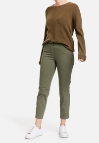 Brun stickad tröja med ribbad textur, matchad med olivgröna slim-fit byxor. Bärs med vita sneakers, vilket skapar en avslappnad outfit.