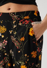 Sorte bukser med svarte blomster som har en rekke fargerike blomster i gult, rødt og hvitt, med en sidelomme og myk, teksturert stoff.