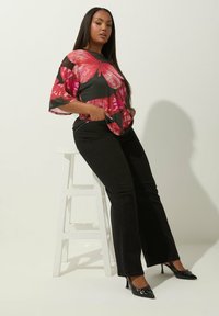 Lyhythihainen paita kukkakuviolla punaisena ja vaaleanpunaisena mustalla taustalla, yhdistettynä mustiin leveisiin farkkuihin ja kiiltäviin mustiin korkokenkiin.