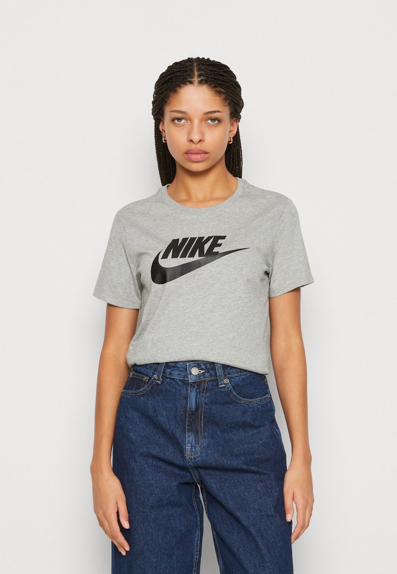 Pilkas medvilninis marškinėlis su juodu Nike logotipu centre, turintis klasikinį apvalų kaklą ir trumpas rankoves, derinamas su tamsiai mėlynomis džinsomis.
