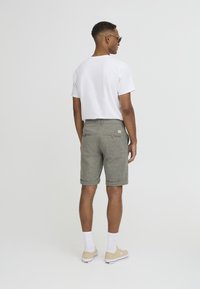 Men's outfit featuring a white t-shirt and gray patterned shorts. The shorts have a textured finish and rolled cuffs, paired with beige sneakers.