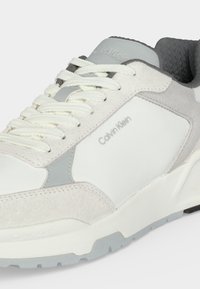 Бели и светлосиви маратонки Calvin Klein с връзки, велурени и платнени панели, текстурирана сива вътрешна подплата и брандирани детайли на страната и езика.