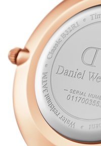 Montre en or rose avec un boîtier métallique lisse, un cadran argenté, des détails gravés et une couronne proéminente. Résistante à l'eau jusqu'à 30 mètres.