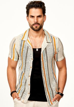 Kurzärmeliges Strickshirt mit einem gemusterten Design, das beige, orange, blaue und graue Streifen sowie braune Knöpfe aufweist und über einem schwarzen Shirt getragen wird.