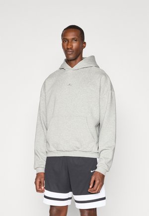 Grey hooded sweatshirt in soft fabric, featuring a front pocket and a small logo at the center. Paired with black shorts with white stripes.