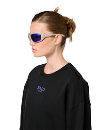 Kobieta z włosami związanymi do tyłu, nosząca beżowe okulary przeciwsłoneczne z niebieskimi szkłami oraz czarną bluzę z nadrukiem "HALO" w kolorze niebieskim na piersi, zwrócona w lewo.