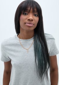 Szürke crew-neck póló, aranylánc keresztfüggővel, hosszú, egyenes haj, türkiz csíkokkal, sima bőr, semleges háttér.