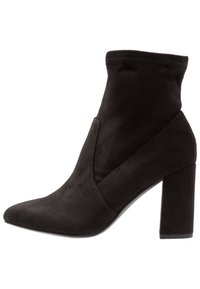 Bottine en daim noir avec un bout pointu, un talon bloc de hauteur intermédiaire et un design de tige élastique. Texture lisse et minimalisme dans les détails.