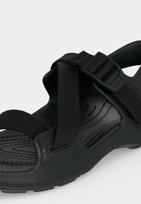 Μαύρο σανδάλι ανοιχτής μύτης με ρυθμιζόμενους υφασμάτινους ιμάντες και υφασμένο πέλμα για καλύτερη πρόσφυση, σχεδιασμένο για casual εξωτερική χρήση.