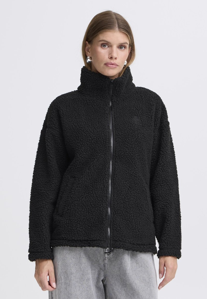 Mustal fleece jakk kõrge kraega ja lukuga. Omab tekstuurset, karvane pinda ja pikki varrukaid.