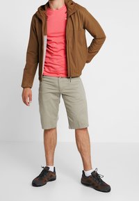 Brown zip-up jacket, pink t-shirt, light beige shorts, and black/brown hiking shoes. Features include hood, casual fit, and visible logo on shirt.