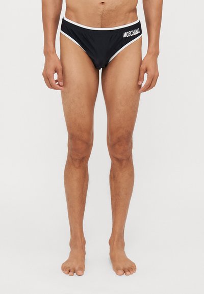 Slip da nuoto neri con accenti bianchi, caratterizzati da un logo sul lato sinistro. Realizzati in un tessuto liscio, presentano un design aderente e a vita bassa.