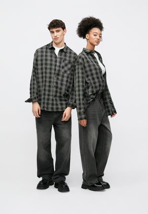 Mustavalkoinen ruudullinen flanellipaita, löysä istuvuus, valkoisten t-paitojen päällä. Molemmilla malleilla on päällään väljät harmaat farkut ja mustat kengät, joissa on paksut pohjat.