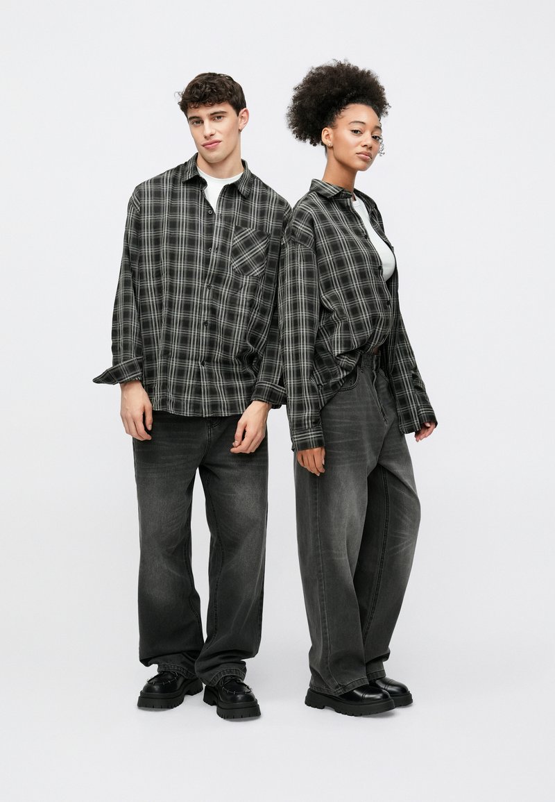 Fekete és szürke kockás flanel ingek, bő szabásúak, fehér pólók fölött viselve. Mindkét modell bőszárú szürke farmert és fekete, vastag talpú cipőt visel.