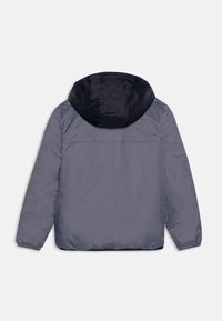 Giacca grigia con cappuccio blu, polsini elasticizzati e design snello. Il tessuto sembra liscio con una leggera lucentezza.