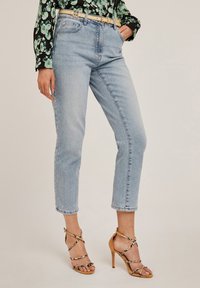 Jasnoniebieskie, wysokie dżinsy o prostym kroju, połączone z beżowymi sandałami na wysokim obcasie z paskami. Gładka tekstura dżinsu, styl casual.