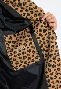 Leopardprint interieurstof in bruin- en zwarttinten, met een zak en branding. De buitenlaag is zwart. Waterafstotend materiaal.