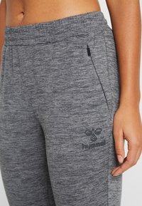 Nærbillede af talje og øvre ben iført grå teksturerede joggingbukser med lynlåslomme og hummel-logo på venstre lår.