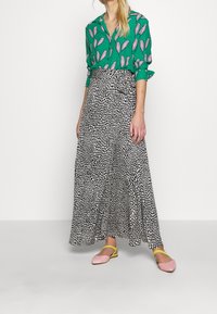 Blusa verde con motivo di foglie rosa, abbinata a una gonna maxi a pois bianco e nero, e ballerine rosa con cinturini gialli.