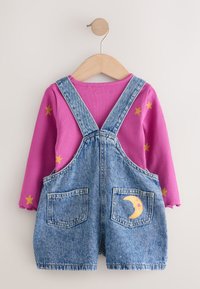 Peto vaquero con camiseta de manga larga rosa. El peto tiene dos bolsillos delanteros y un bordado de luna; la camiseta presenta detalles de estrellas doradas.