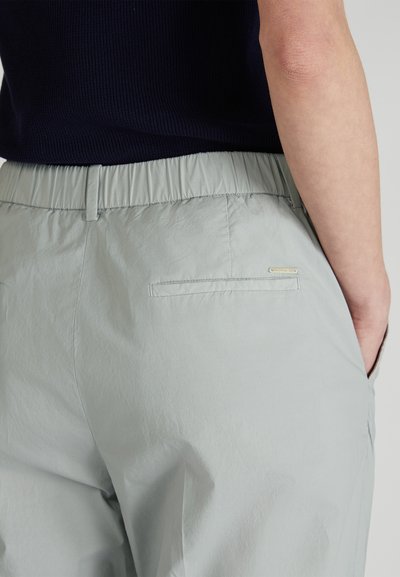 Pantalons taille élastique gris clair avec une texture lisse, dotés de poches arrière et d'un petit logo en métal près de la taille.
