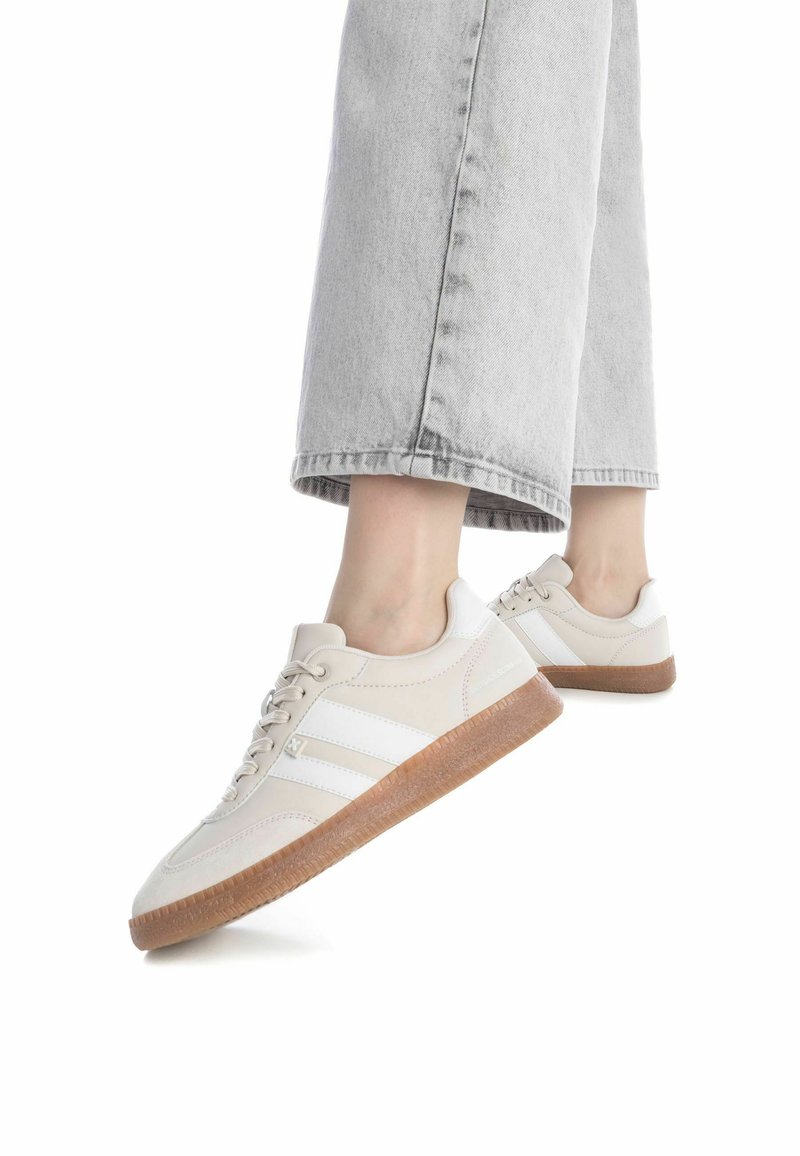 Zapatillas beige con franjas blancas, suelas de goma y cierre de cordones. Material superior suave con costuras resistentes y una suela texturizada.