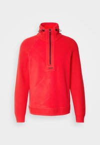 Pull-over en polaire rouge avec col montant, demi-fermeture éclair noire à l'avant, cordons réglables, poignets et ourlet côtelés, et petit logo "BOSS" sous la fermeture éclair.