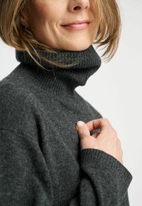 Pulover turtleneck de culoare gri cărbune, realizat dintr-un material tricotat moale, având un guler și manșete răsucite, cu o croială lejeră și o textură subtilă.