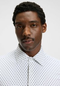 Witte shirt met een geometrisch marineblauw patroon, puntige kraag en knoopsluiting aan de voorkant. Katoenen materiaal met een soepele textuur.