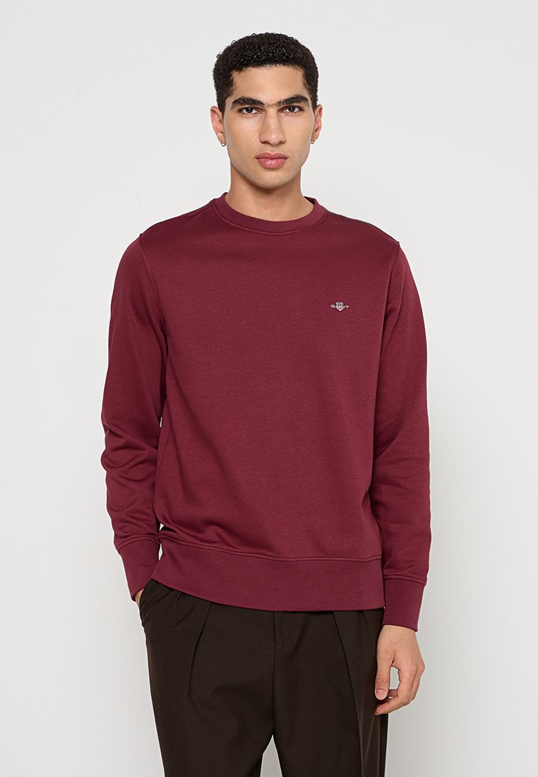 Sudadera burdeos con cuello redondo, mangas largas y puños acanalados. Presenta un pequeño logo bordado en el pecho. Textura suave.