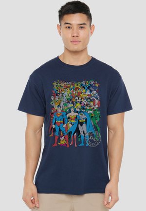 Young man wearing navy blue T-shirt with colorful DC Comics superheroes including Superman, Wonder Woman, and Batman on front.