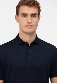 Himmelblaues Polohemd aus weichem Strickstoff, mit klassischem Kragen und einer Knopfleiste mit drei Knöpfen. Strukturierte Oberfläche mit subtilen Variationen.