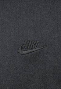 Ciemnoszara tkanina z czarnym haftowanym logo Nike, na środku z nazwą marki i symbolem łyżwy.