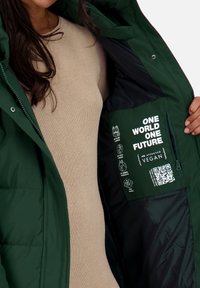 Chaqueta acolchada verde con un bolsillo con cremallera que presenta texto e íconos blancos, fabricada con materiales veganos; el interior es negro con una textura suave.