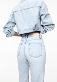 Veste en jean bleu clair courte avec manches retroussées, associée à un jean taille haute bleu clair avec une poche arrière unie et une pièce en patch.