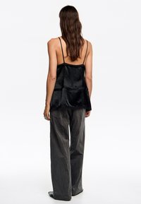Top negro sin mangas con un diseño en capas, hecho de una tela suave. Combinado con pantalones grises sueltos y texturizados. Sandalias negras sencillas visibles.