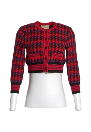 Chaqueta corta de pata de gallo en rojo, negro y azul con botones negros, mangas largas y dos bolsillos delanteros sobre un torso de maniquí blanco.