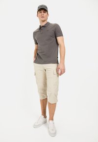 Grijze polo, beige cargo shorts en witte sneakers. De polo heeft een subtiele logo; de shorts hebben zijzakken en een relaxte pasvorm.