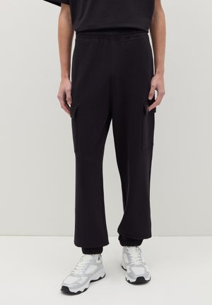 Schwarze Cargo-Hosen mit elastischem Bund, zwei Seitentaschen und gerippten Säumen. Aus weichem Material, geeignet für legere Trageanlässe.