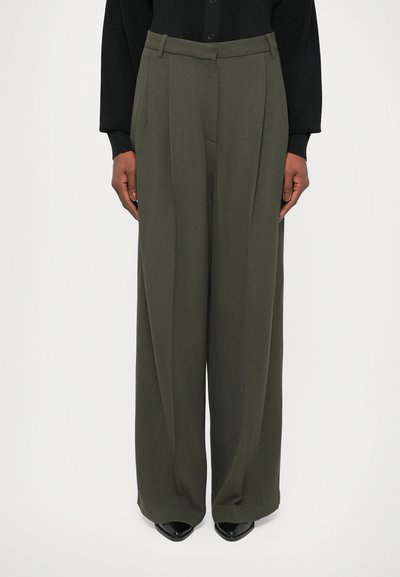 Pantaloni a gamba larga in verde oliva, con tessuto testurizzato, pieghe e una vita tailored. Abbinati a scarpe nere a punta.
