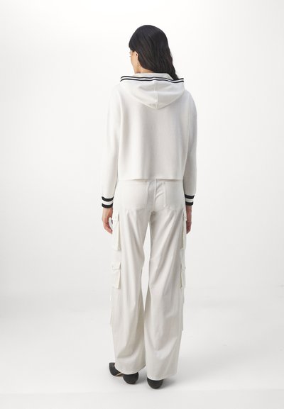 Un hoodie blanc court avec un col à rayures noires, assorti à un pantalon cargo blanc à jambes larges, avec des poches latérales et des ourlets évasés.