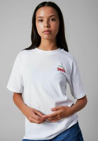 Vit t-shirt med kort ärm som har en liten körsbärsgrafik på vänster bröst. Tillverkad av bomull, med en avslappnad passform och mjuk textur.